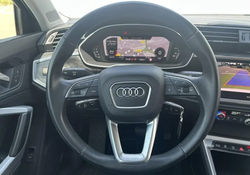 Vue intérieure centrée sur le volant noir multifonctions d’un Audi Q3 2022 avec tableau de bord numérique et écran de caméra de recul.