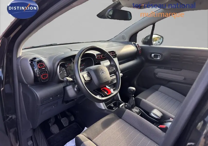 Vue intérieure côté conducteur du Citroën C3 Aircross noir, avec volant multifonction et détails rouges sur les aérateurs.