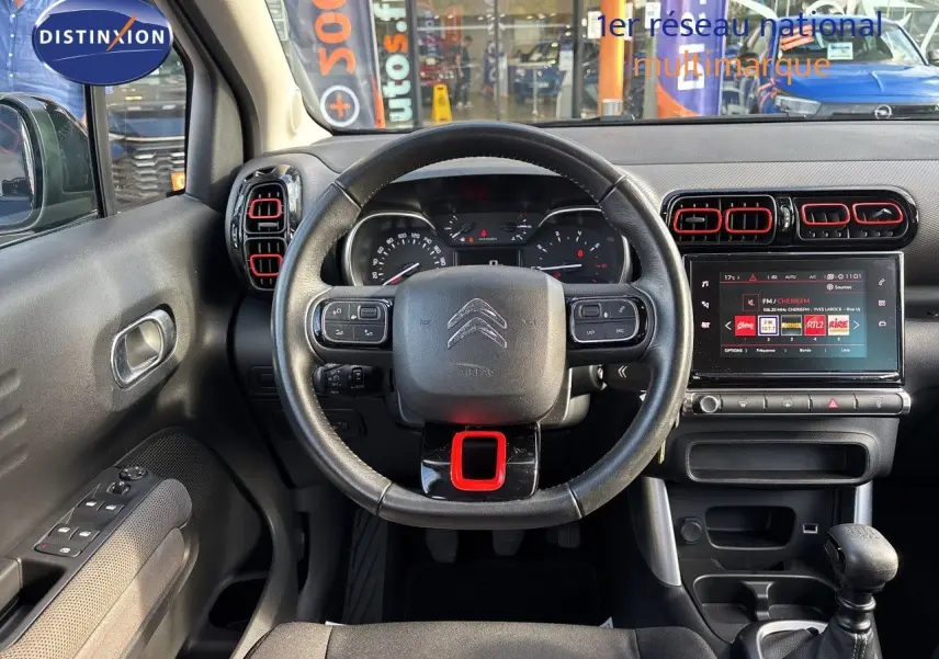 Intérieur de Citroën C3 Aircross 2019, vue frontale du volant noir avec touches rouges et écran tactile central allumé.