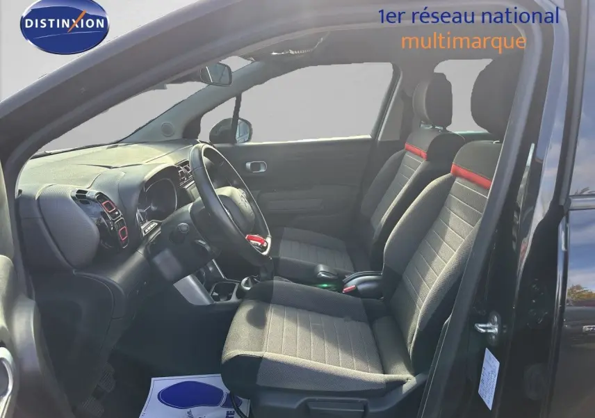 Vue intérieure côté conducteur d’un Citroën C3 Aircross noir Perla Metal 2019, sièges tissu noir avec bande rouge.