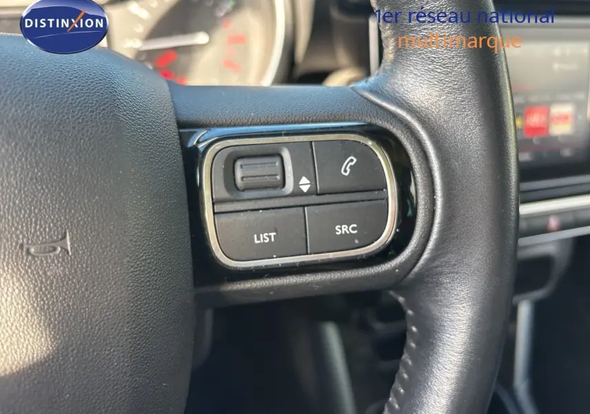 Gros plan sur les commandes gauche du volant en cuir noir du Citroën C3 Aircross 2019, intérieur moderne et écran tactile en arrière-plan.
