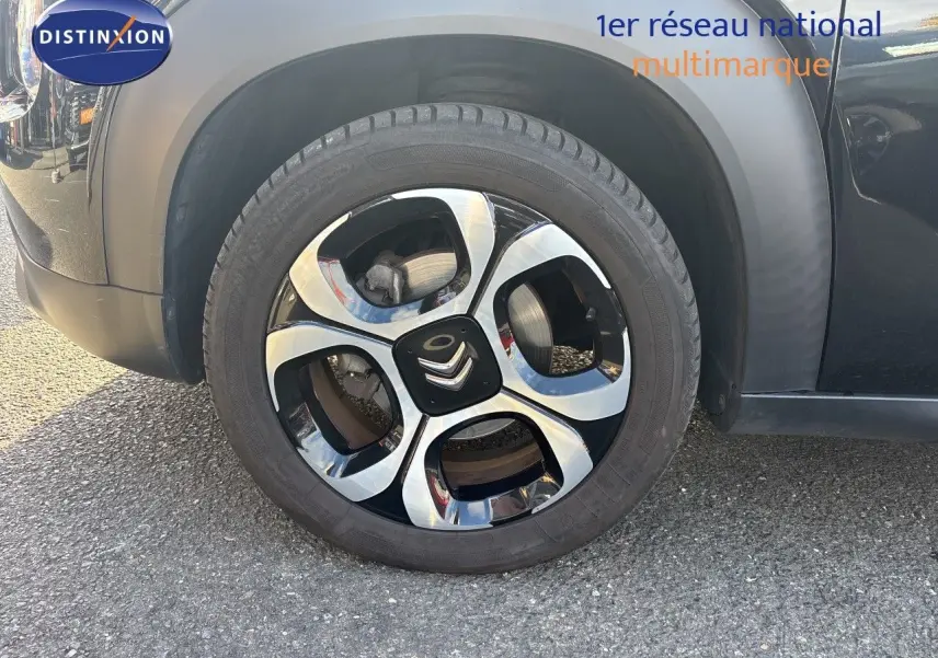 Gros plan sur la roue avant gauche d'une Citroën C3 Aircross noir perla metal avec jante alliage bicolore distinctive.