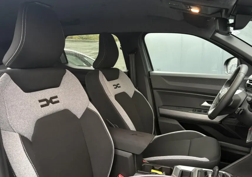 Vue intérieure côté droit du Dacia Duster 2026, sièges bi-matière gris clair et noir avec logo distinctif brodé.