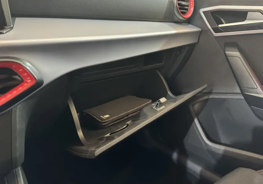 Intérieur de la SEAT Ibiza 2024 rouge, vue côté passager sur la boîte à gants ouverte avec livret noir.