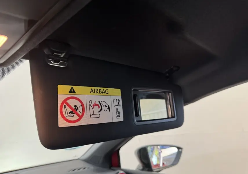 Vue intérieure du pare-soleil côté conducteur avec miroir et avertissement airbag, rétroviseur extérieur rouge visible.