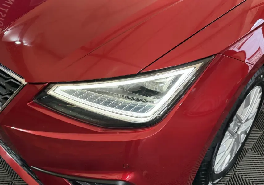 Gros plan sur le phare avant droit allumé d’une SEAT Ibiza 1.0 TSI 110 FR rouge 2024 avec jante alu visible.