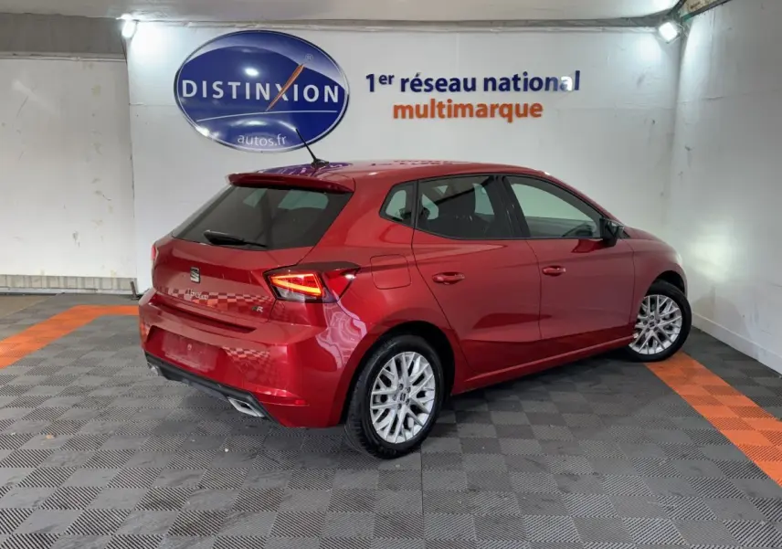 Vue 3/4 arrière droite d'une SEAT Ibiza 1.0 TSI 110 FR rouge brillante avec jantes alliage et feux LED allumés.
