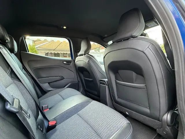 Vue intérieure arrière côté gauche de la Renault Clio V bleu iron, montrant les sièges tissu et cuir noir.