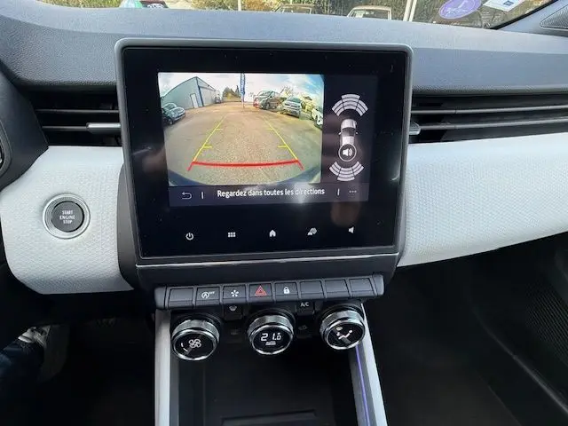 Vue intérieure du tableau de bord de la Renault Clio V bleu Iron, écran tactile affichant la caméra de recul et commandes de climatisation.