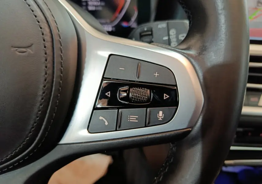 Gros plan sur les commandes multifonctions argentées du volant cuir noir d'une BMW Série 3 318d 2022.