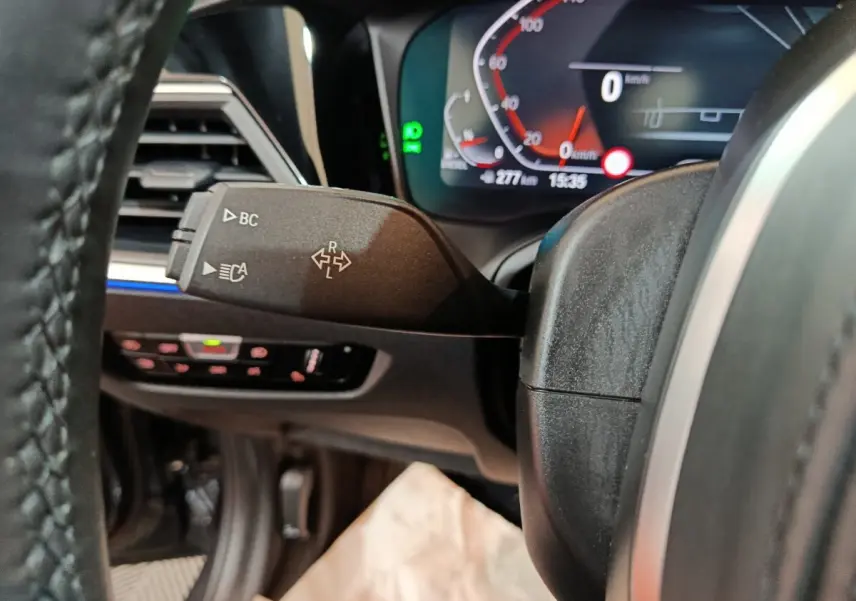 Gros plan sur la manette de clignotant à gauche du volant noir, avec tableau de bord numérique BMW Série 3 318d.