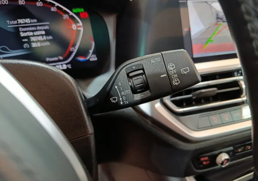 Gros plan sur la manette d'essuie-glace côté gauche du tableau de bord d'une BMW Série 3 gris clair, avec affichage numérique en arrière-plan.