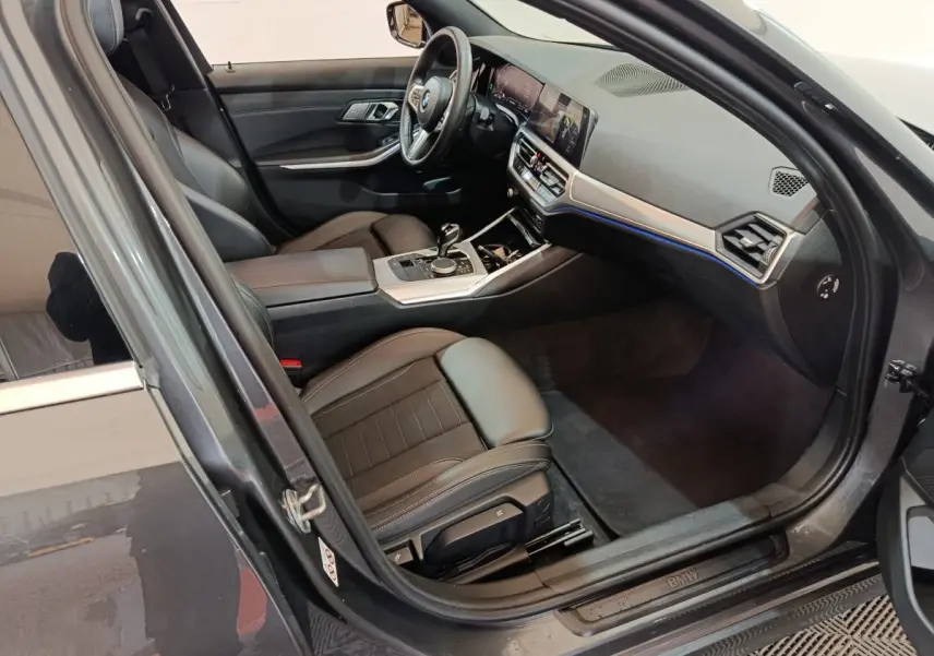 Vue intérieure côté conducteur d'une BMW Série 3 318d grise, avec tableau de bord moderne et sièges en cuir noir.