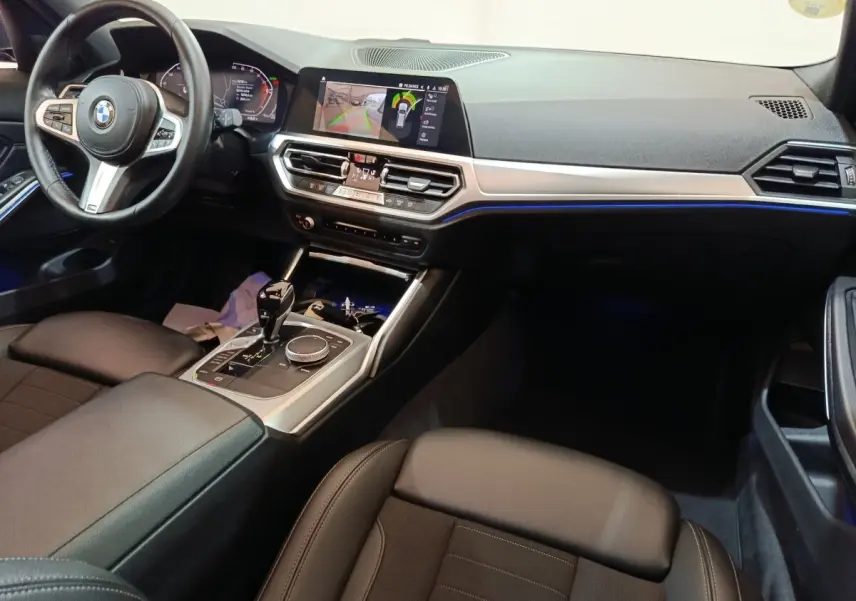 Vue intérieure côté conducteur de la BMW Série 3 318d Lounge 2022, avec tableau de bord digital et éclairage d'ambiance bleu.