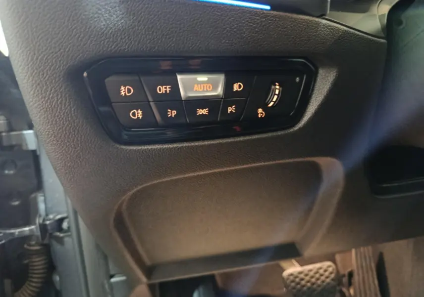 Gros plan sur les commandes d’éclairage à gauche du volant dans une BMW Série 3 gris clair 318d Lounge 2022.