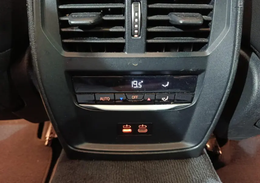 Détail de la console arrière noire avec commandes climatisation digitale et prises USB rouges sur BMW Série 3 gris clair.