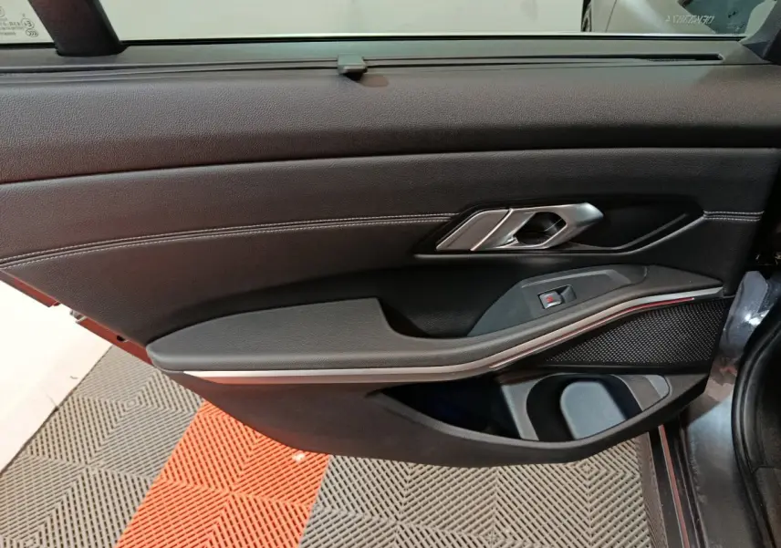Vue intérieure côté droit de la porte d’une BMW Série 3 gris clair, avec garniture noire et poignée métal.