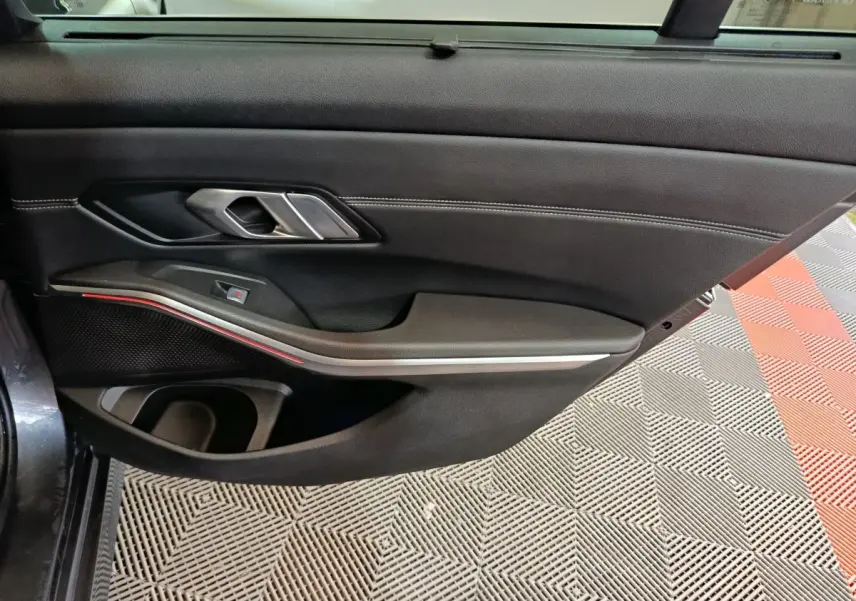 Vue intérieure du panneau de porte côté conducteur de BMW Série 3 gris clair, avec poignée argentée et bande lumineuse rouge.