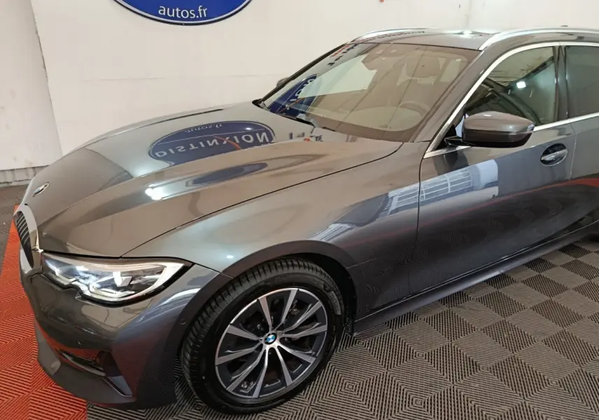 BMW Série 3 318d gris clair vue 3/4 avant droit, mettant en valeur ses phares LED et jantes alliage.