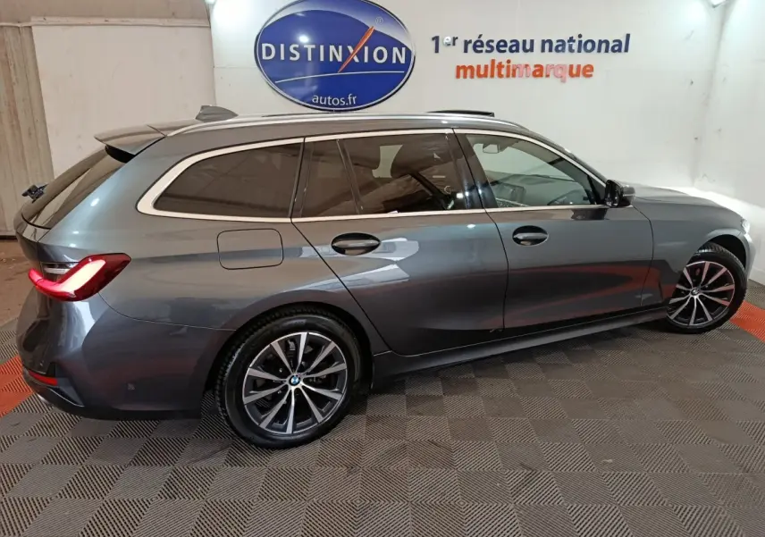 BMW Série 3 Touring gris clair vue de profil côté droit, avec feux arrière allumés dans un showroom.