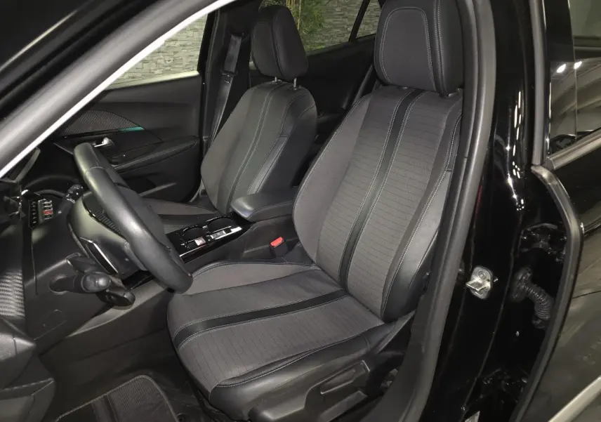 Vue intérieure côté conducteur du Peugeot 2008 noir 2021, sièges tissu et cuir gris avec surpiqûres bleues.