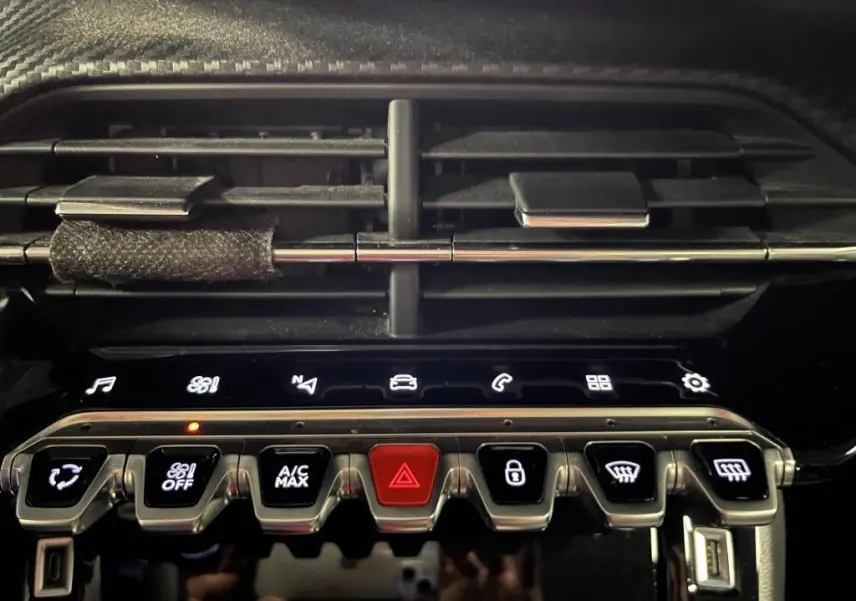 Gros plan sur la console centrale du Peugeot 2008 noir, avec commandes tactiles et aérateurs horizontaux noirs.