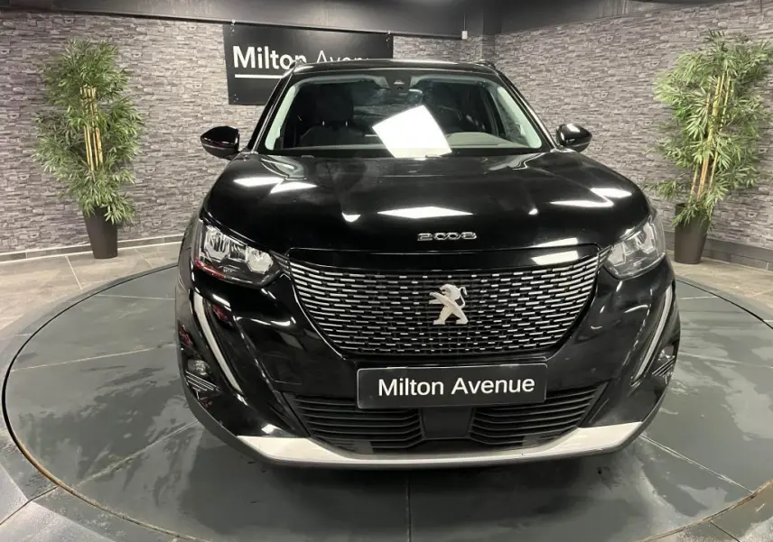 Vue avant d'un Peugeot 2008 noir Perla Nera avec calandre chromée et logo lion sur fond de showroom.