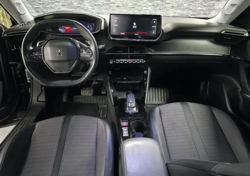Vue intérieure avant du Peugeot 2008 2021 noir, planche de bord carbone et volant compact cuir avec commandes intégrées.