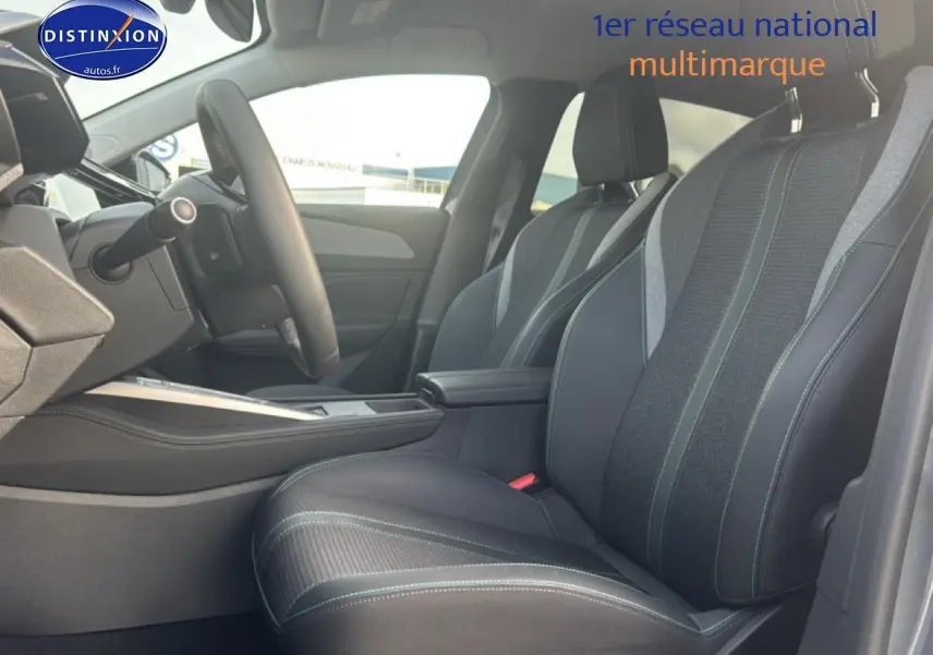 Vue intérieure côté conducteur de la Peugeot 308 2024 avec sièges tissu et cuir noirs et accoudoir central.