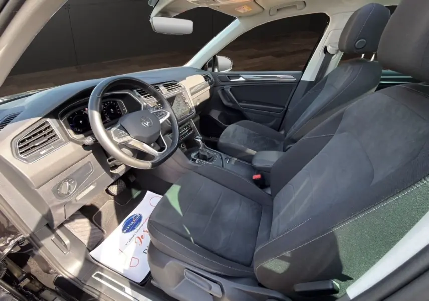 Vue intérieure côté conducteur du Volkswagen Tiguan 2.0 TDI noir, avec volant cuir et écran tactile central.