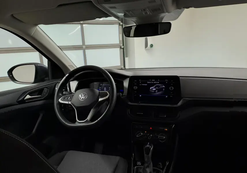 Vue intérieure du poste de conduite du Volkswagen T-Cross gris cendré, avec volant multifonction et écran tactile central allumé.
