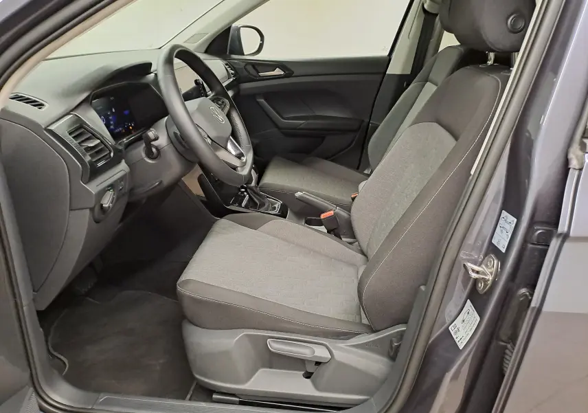 Vue intérieure côté conducteur du Volkswagen T-Cross gris cendré 2025, montrant sièges tissu et tableau de bord moderne.