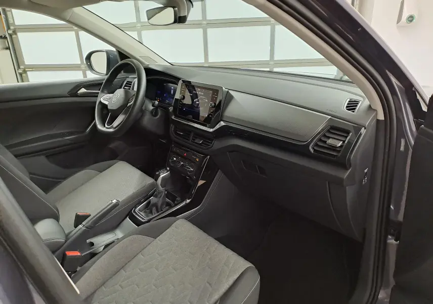 Vue intérieure côté conducteur du Volkswagen T-Cross 2025, avec tableau de bord moderne et sièges gris tissu.