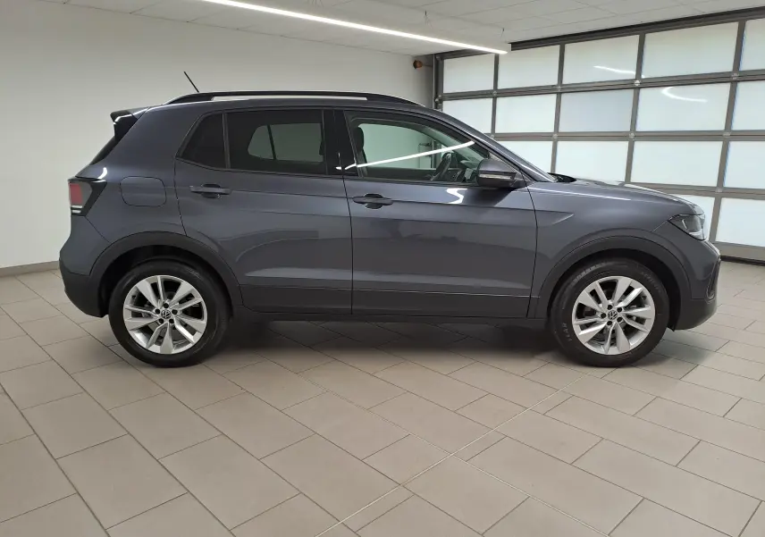 Vue de profil côté gauche d'un Volkswagen T-Cross 2025 gris cendré avec jantes alliage et toit noir.