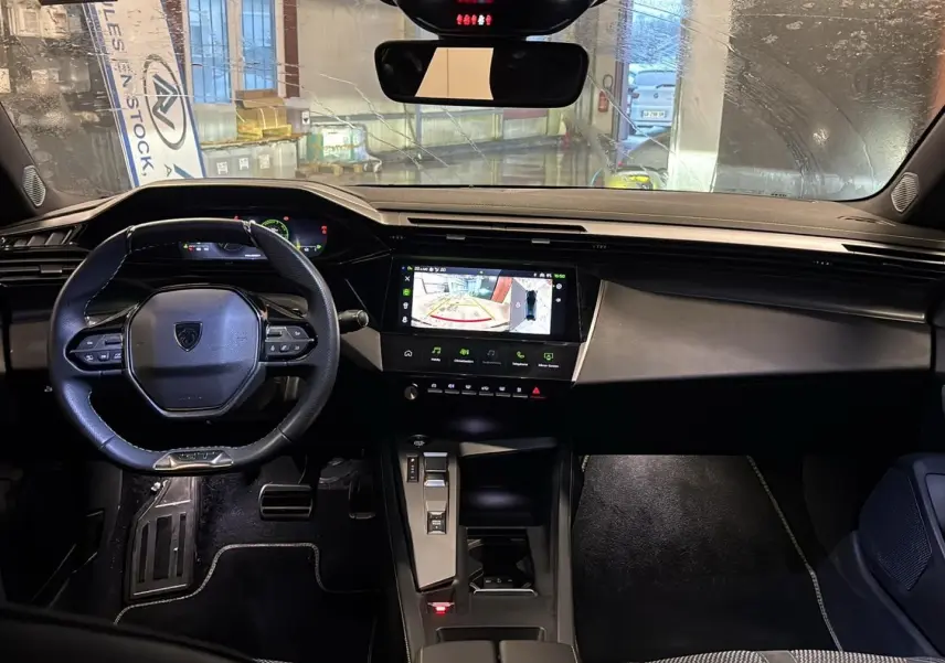 Intérieur noir de la Peugeot 408 Hybrid 145 GT, vue de face sur le tableau de bord avec écran tactile et volant cuir.