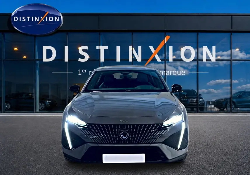 Vue avant d'une Peugeot 408 Hybrid 145 GT gris sélénite avec phares LED allumés devant une vitrine Distinxion.