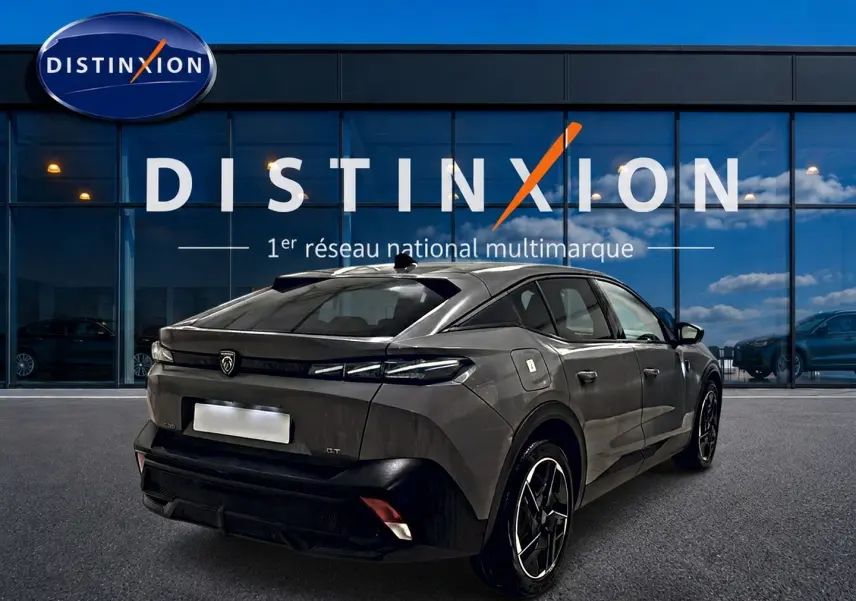 Vue 3/4 arrière droite d'une Peugeot 408 Hybrid 145 GT gris sélénite avec jantes alu noires devant une vitrine Distinxion.