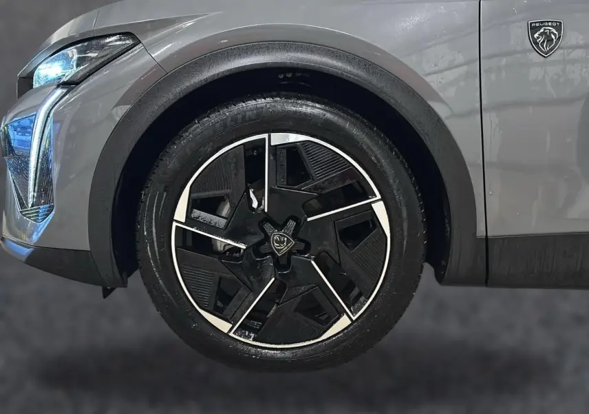 Gros plan sur la roue avant droite et le logo Peugeot d’une 408 Hybrid gris sellenium avec phares LED allumés.