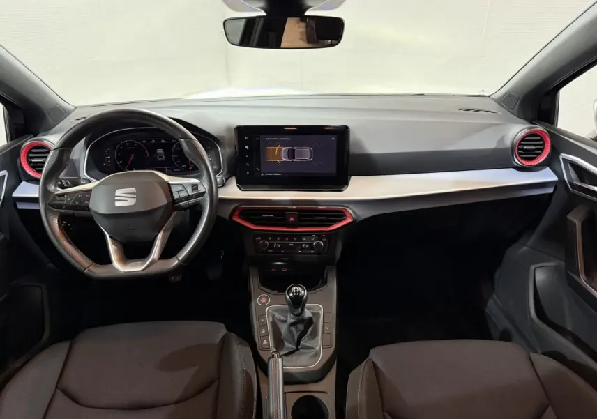 Vue intérieure frontale du tableau de bord noir et gris avec volant cuir alu et touches rouges sur les aérateurs du SEAT Ibiza 2024.
