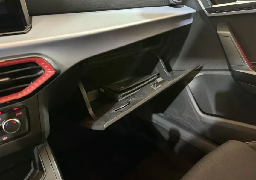 Intérieur de la SEAT Ibiza 2024 noir, vue sur la boîte à gants ouverte avec un livret à l’intérieur et détails rouges autour des aérateurs.