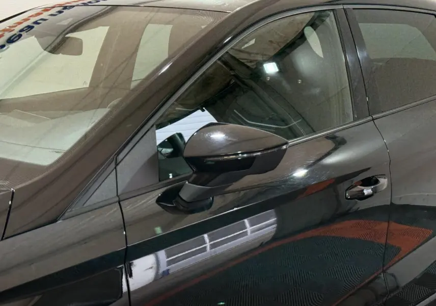 Vue rapprochée du côté gauche d’une SEAT Ibiza 1.0 TSI 110 FR noire, mettant en valeur le rétroviseur et la poignée de porte.