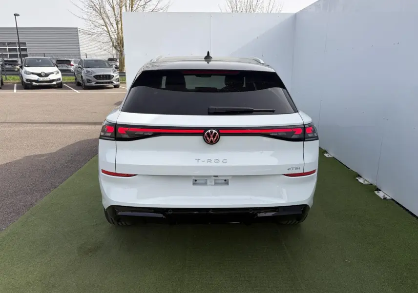 Vue arrière du Volkswagen T-Roc blanc pur avec toit noir et bandeau lumineux LED reliant les feux arrière.