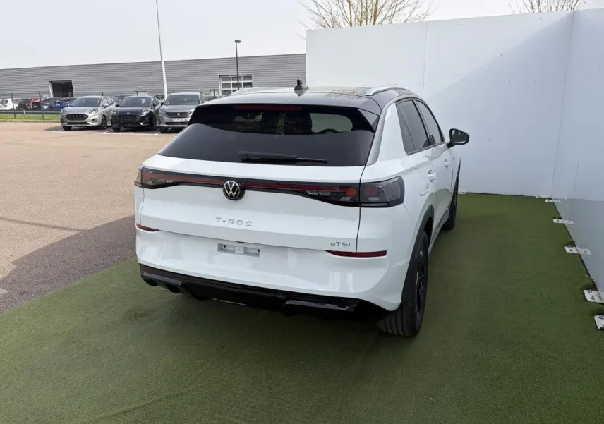 Vue 3/4 arrière droite du Volkswagen T-Roc blanc pur avec toit noir et feux arrière LED reliés par un bandeau lumineux.