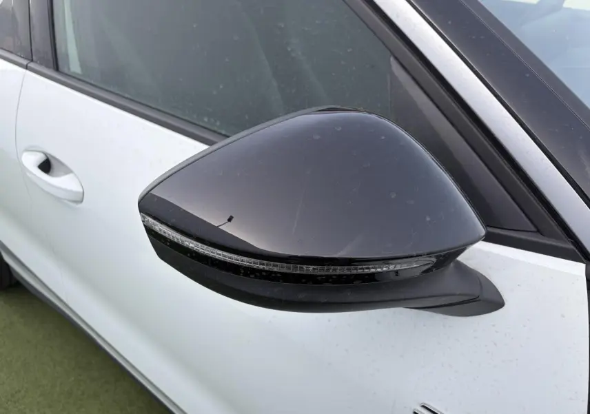 Rétroviseur noir côté gauche en gros plan sur Volkswagen T-Roc blanc pur avec toit noir, vue partielle de la porte avant.