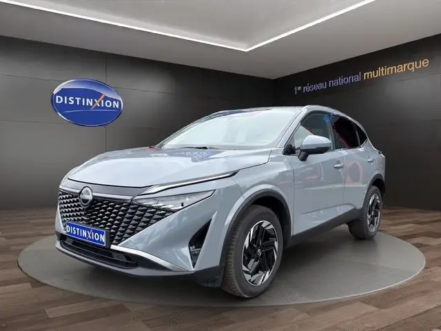 Vue 3/4 avant d’un Nissan Qashqai gris foncé exposé en showroom avec calandre noire et jantes stylisées.
