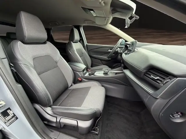 Vue intérieure côté conducteur du Nissan Qashqai 2025 gris foncé, montrant sièges tissu et tableau de bord moderne.