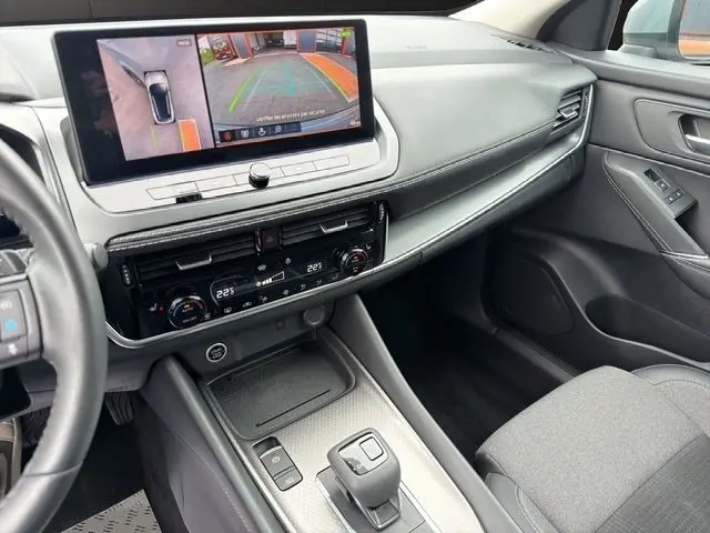 Vue intérieure côté passager du tableau de bord et console centrale du Nissan Qashqai gris foncé avec écran tactile et commandes climatisation.