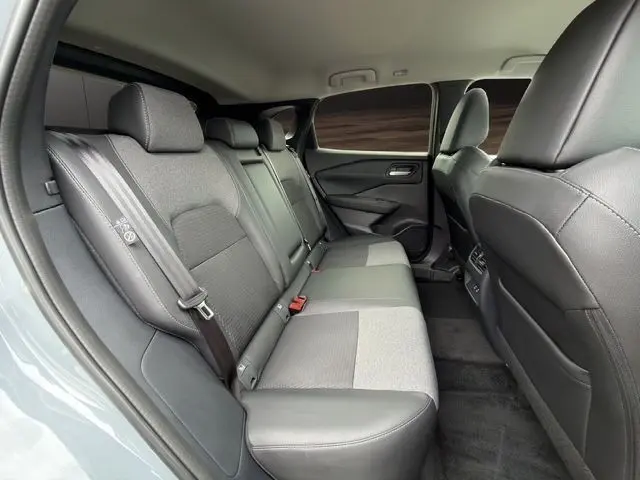 Vue intérieure arrière droite du Nissan Qashqai 2025 gris foncé, montrant la banquette 3 places en tissu et cuir avec ceintures de sécurité.