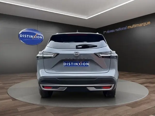 Vue arrière d'un Nissan Qashqai gris foncé 2025 avec feux LED et logo Distinxion en arrière-plan.
