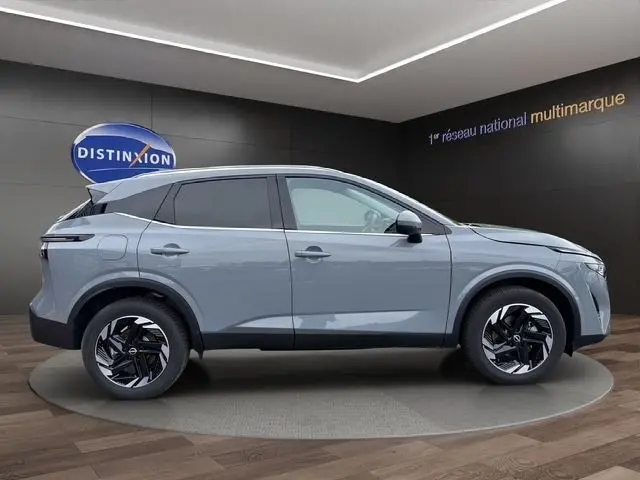 Vue latérale droite d'un Nissan Qashqai gris foncé 2025 avec jantes noires et toit noir dans un showroom.